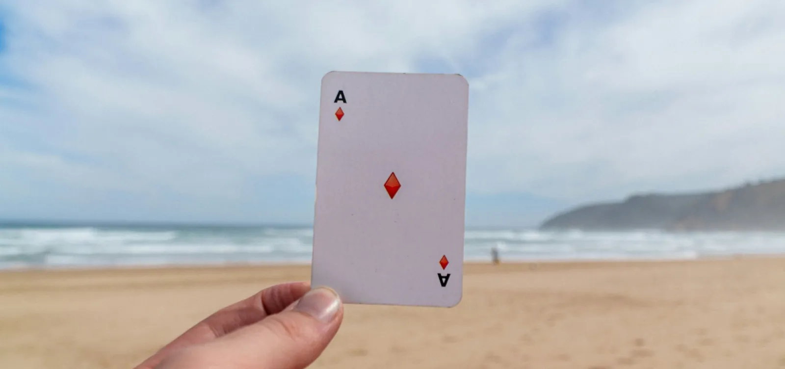 An ace of diamonds held up against a beach and sea