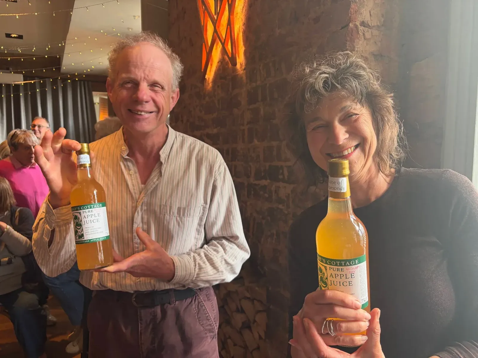 Two prize winners smiling and holding bottles of Days Cottage apple juice
